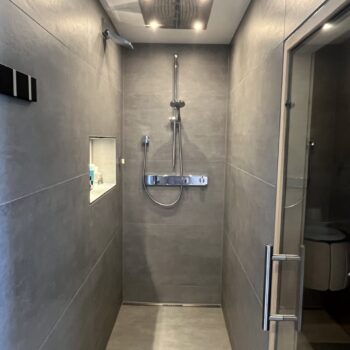Barrierefreie Walk-in-Dusche mit Regenduschkopf, großformatigen anthrazitfarbenen Fliesen, Glasduschwand und moderner Unterputz-Duscharmatur im stilvollen Badezimmer.